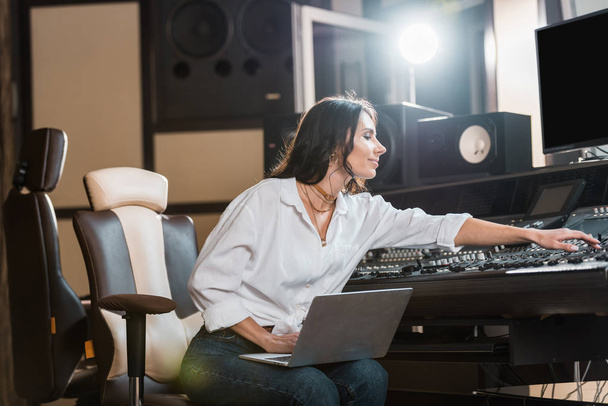 producteur sonore attrayant et souriant utilisant un ordinateur portable et travaillant à la console de mixage en studio d'enregistrement
 - Photo, image