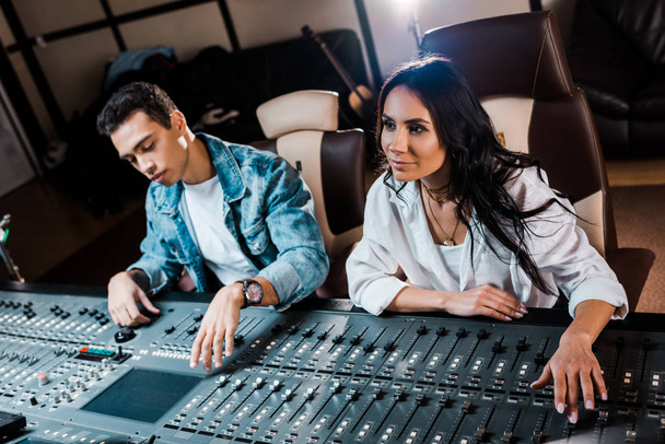 two young attentive multicultural sound producers working at mixing console in recording studio - Photo, Image