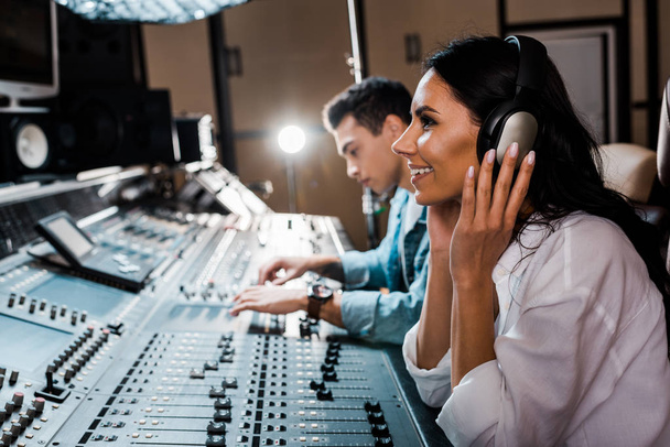 smiling woman sitting in headphones in recording studio  - Фото, зображення
