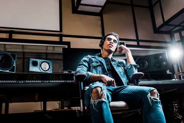 attentive mixed race sound producer in headphones listening music in recording studio - Foto, Bild