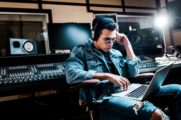 concentrado produtor de som de raça mista em fones de ouvido usando laptop em estúdio de gravação
 - Foto, Imagem