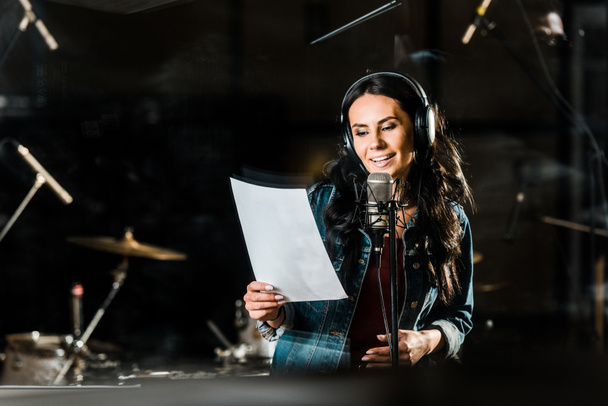 beautiful woman in headphones singing in recording studio near microphone - Photo, Image