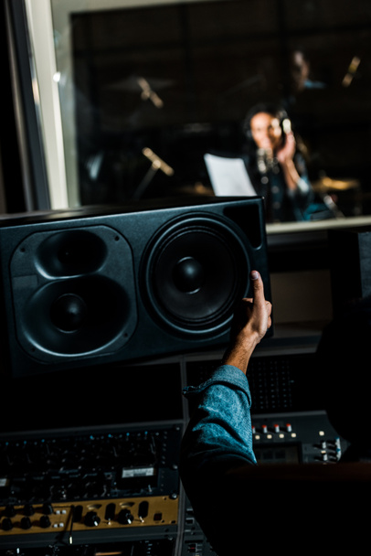 selective focus of mixed race sound producer showing thumb up to woman singing in recording studio - Foto, imagen