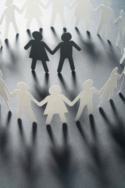 Paper figure of a couple surrounded by circle of paper people holding hands on white surface. Bulling, minorities, conflict concept. - Photo, Image