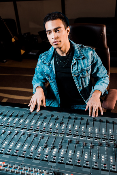 concentrated mixed race sound producer working at mixing console in recording studio - Photo, Image