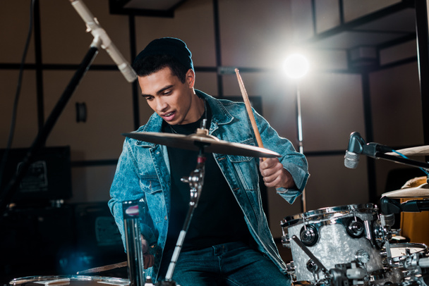 handsome, inspired mixed race musician playing drums in recording studio - Photo, Image