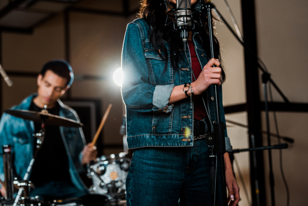 enfoque selectivo de la mujer cantando en el estudio de grabación mientras músico de raza mixta tocando la batería
 - Foto, imagen