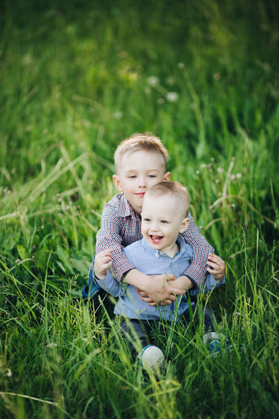 Kaksi pientä onnellista veljeä farkuissa ja tarkastetuissa paidoissa kävelemässä puistossa
. - Valokuva, kuva