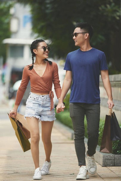 Onnellinen nuori pari kädestä kävellessään ulkona ostoskassien kanssa
 - Valokuva, kuva