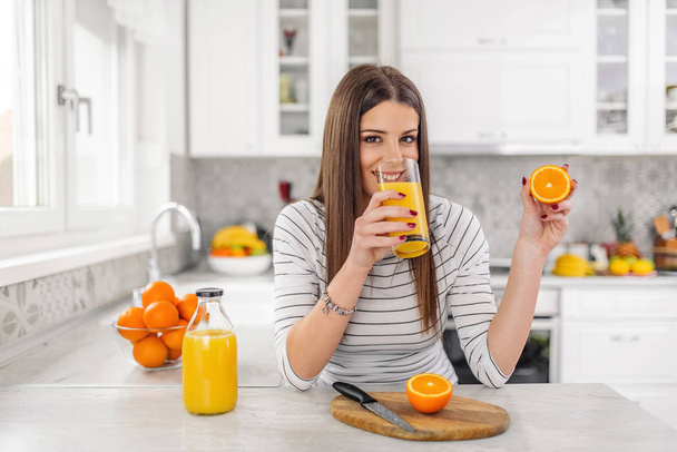 Close up Atractiva joven mujer bebiendo jugo mientras sostiene la fruta naranja en rodajas
. - Foto, Imagen