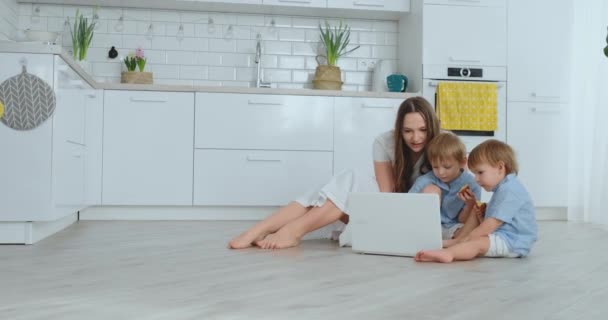 Çocuklarla oturma odasında katta oturan ve dizüstü bilgisayar ekranına bakarak genç güzel anne - Video, Çekim