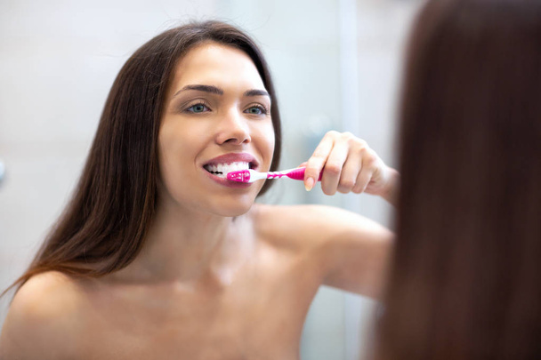 Chica de pie frente al espejo y cepillarse los dientes
 - Foto, Imagen