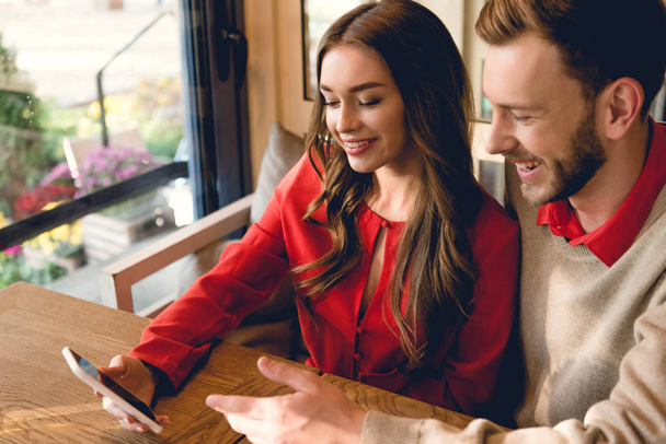 happy man looking at smartphone near attractive woman in cafe  - Foto, imagen