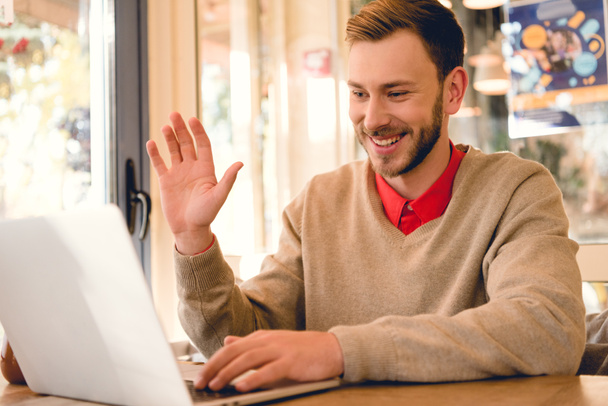alegre freelancer saludando la mano mientras tiene videollamada en el ordenador portátil
  - Foto, Imagen