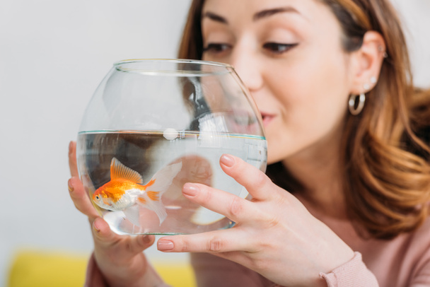 красивая молодая женщина держит аквариум с яркой золотой рыбой
 - Фото, изображение