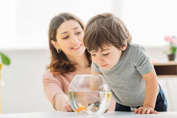 selective focus of adorable child looking into fish bowl near smiling mother - Фото, зображення