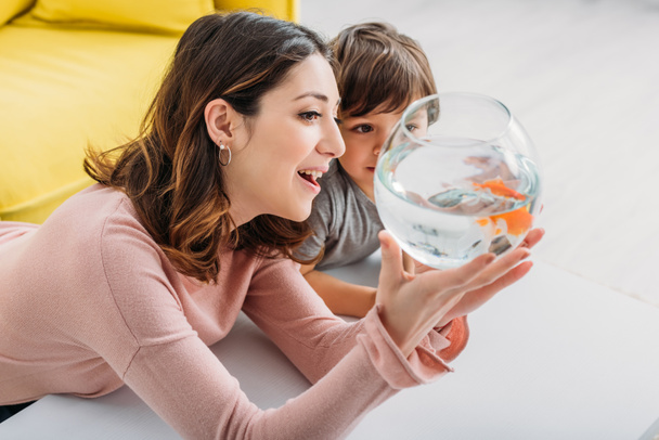smiling attractive woman showing fish bowl to adorable son - Photo, Image