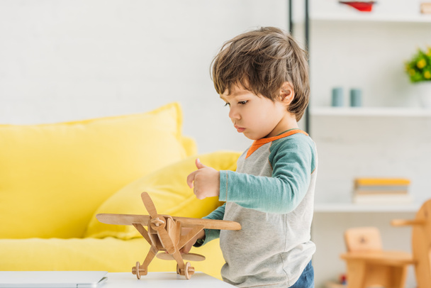 cute attentive boy playing with wooden plane model at home - Foto, Imagem