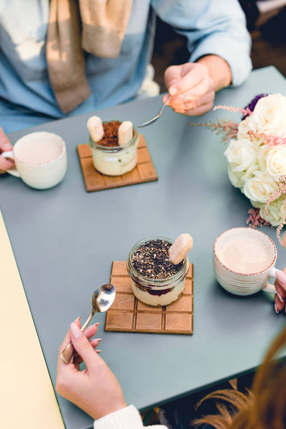 overhead view of man and woman holding spoons near desserts and cups in cafe  - Foto, imagen
