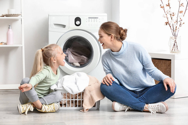 Νεαρή γυναίκα και η μικρή κόρη της παίζοντας στο σπίτι την ημέρα της πλυντηρίου - Φωτογραφία, εικόνα