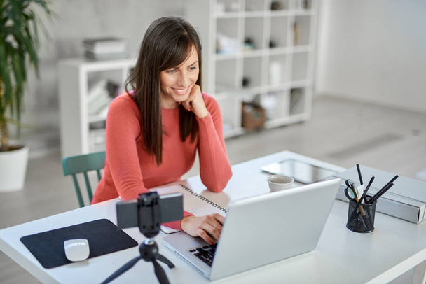 Beautiful smiling Caucasian businesswoman sitting in modern office and using laptop. - Foto, imagen