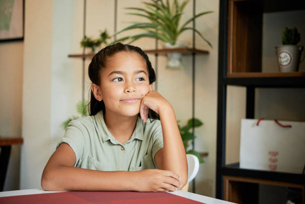 Édes ázsiai lány, gondolkodás, és keres el hangulatos kávézó asztalnál ülve - Fotó, kép