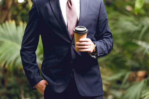 bijgesneden beeld van zakenman in pak en stropdas houdende koffie te gaan in Oranjerie - Foto, afbeelding