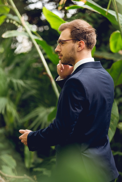 zakenman in pak en bril praten op smartphone in kas en op zoek weg - Foto, afbeelding