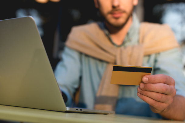 vista recortada del hombre que sostiene la tarjeta de crédito mientras utiliza el ordenador portátil
  - Foto, imagen