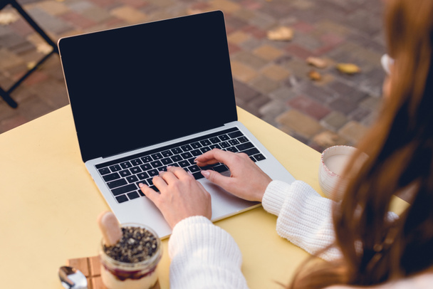 bijgesneden weergave van jonge vrouw te typen op laptop met leeg scherm in de buurt zoete dessert  - Foto, afbeelding