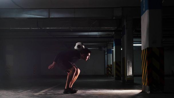 Underground parking lot. A soccer man training his football skills. Catching the ball on his back. - Foto, Bild