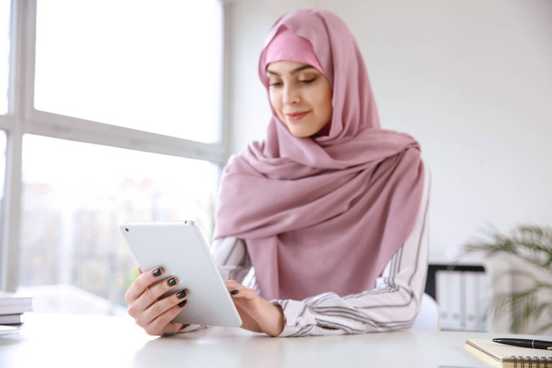 Νεαρή μουσουλμανική γυναίκα με tablet υπολογιστή στο τραπέζι - Φωτογραφία, εικόνα