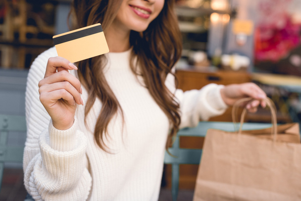 vista recortada de la niña feliz sosteniendo la tarjeta de crédito y bolsas de compras
  - Foto, imagen
