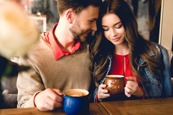 щасливий бородатий чоловік дивиться на привабливу дівчину, тримаючи чашку кави
 - Фото, зображення