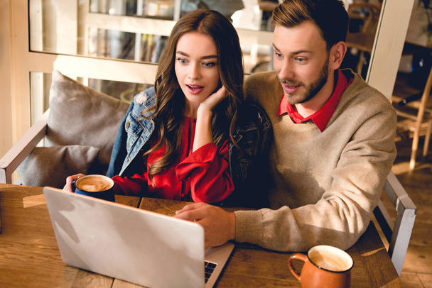 verrast man en mooie jonge vrouw te kijken naar laptop in café  - Foto, afbeelding