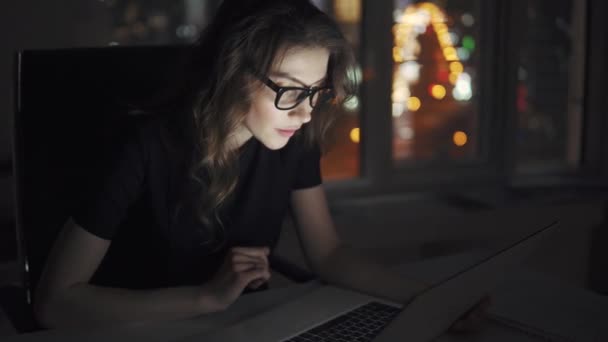 portrét mladé atraktivní obchodní žena pracující na přenosném počítači v podvečer v kanceláři. dívka v obleku a brýle na pozadí světla noční město - Záběry, video