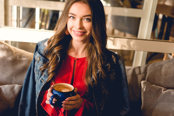 iloinen nuori nainen tilalla kuppi kahvia ja hymyilee kahvilassa
  - Valokuva, kuva