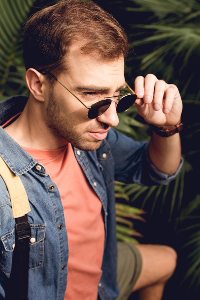 guapo turista tocando gafas de sol en bosque tropical
 - Foto, Imagen