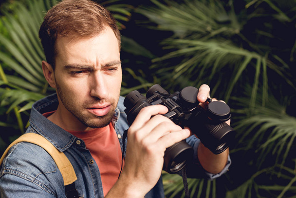 handsome tourist with binoculars looking away in tropical forest - Photo, image