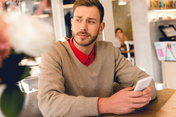 handsome bearded man holding smartphone in cafe  - Фото, зображення