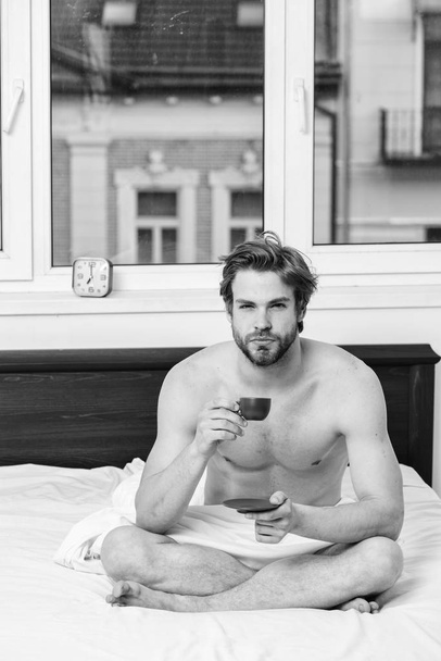 Coffee fills you with energy. Every morning with his coffee. Begin good day. How coffee affects your body from first sip. Man handsome macho with muscular torso relaxing on bed with cup of coffee - Fotografie, Obrázek