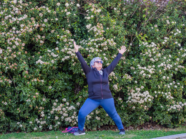 Starší žena s bílými vlasy trénuje gymnastiku v městském parku - Fotografie, Obrázek