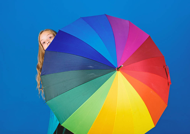 Girl cheerful hide behind umbrella. Colorful umbrella accessory. Weather forecast concept. Stay positive though rainy day. Brighten up life. Kid peek out colorful rainbow umbrella. Color your life - Фото, зображення
