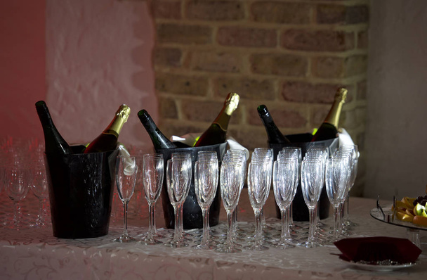Empty glasses on the table,A row of empty champagne glasses.Furshet, catering.Glasses for champagne or wine.Still life with cooled champagne bottle standing in a bucket with ice and glasses in blurry - Photo, Image