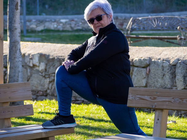 Μια ηλικιωμένη γυναίκα με λευκά μαλλιά που εξασκούνται στη γυμναστική σε ένα αστικό πάρκο - Φωτογραφία, εικόνα
