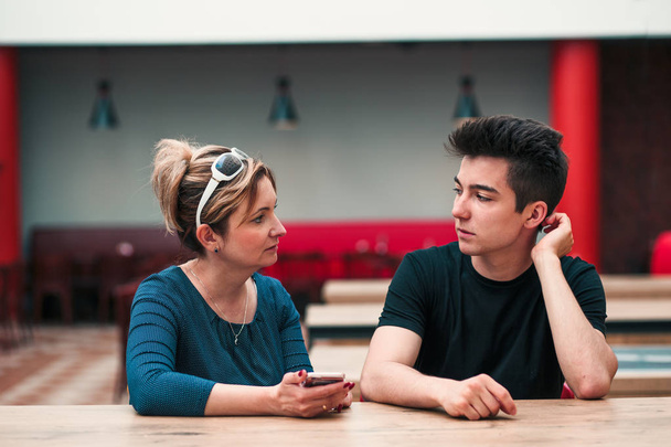 Vrouw en jonge man praten met elkaar en het gebruik van mobiele telefoons - Foto, afbeelding