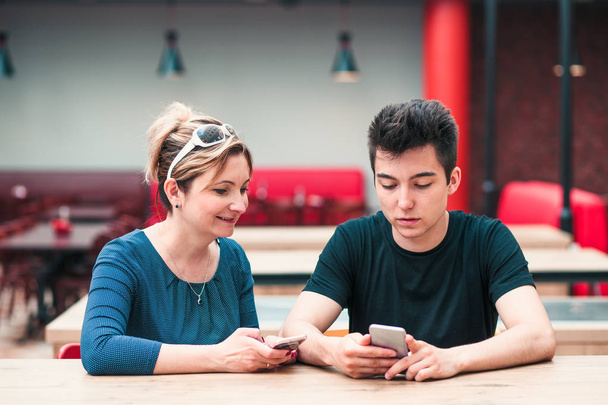 Žena a mladý muž, kteří spolu hovoří a používají mobilní telefony - Fotografie, Obrázek