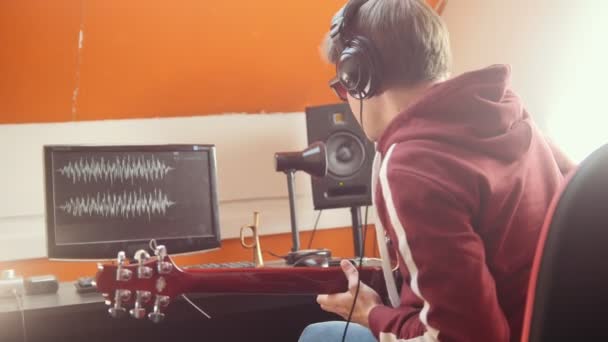 Um músico com auscultadores a tocar guitarra e a gravar o som no estúdio. Olhando para o monitor
 - Filmagem, Vídeo