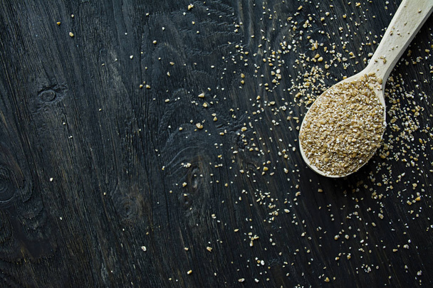 Wheat groats in a wooden spoon on a wooden dark background. Wooden spoon with wheat grains. - Foto, afbeelding