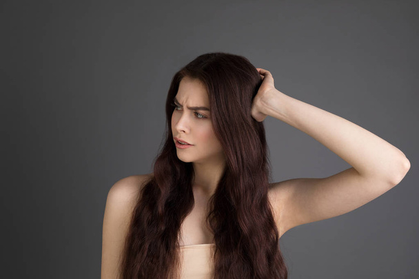 Portrait de jeune fille brune mécontente touchant les cheveux
 - Photo, image